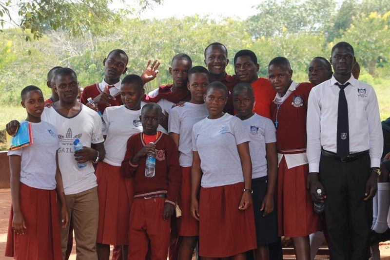 A group of students in uniform pose with Enock on a sunny day.