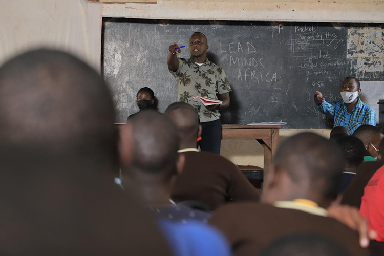 A teacher pointing to a student with their hand raised in a classroom setting.