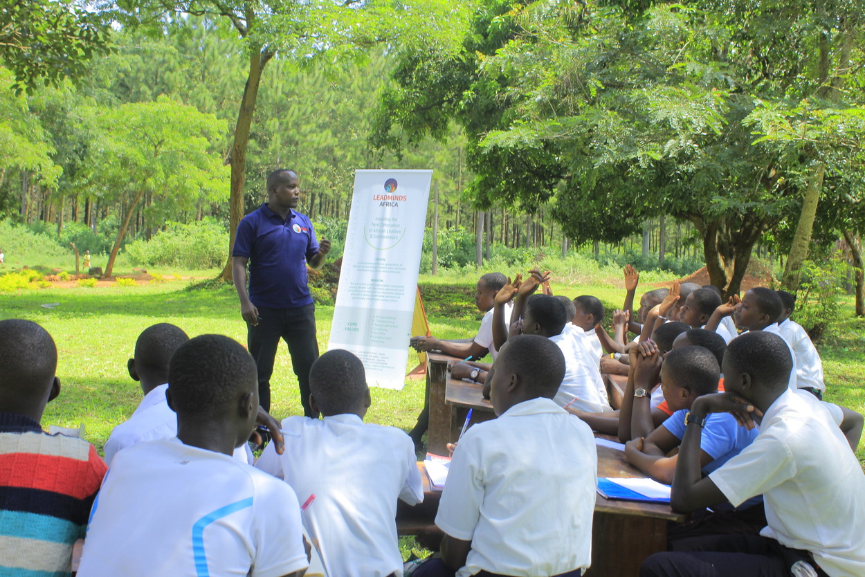 Our founder Enock teaching students outside under a tree in the sunlight.