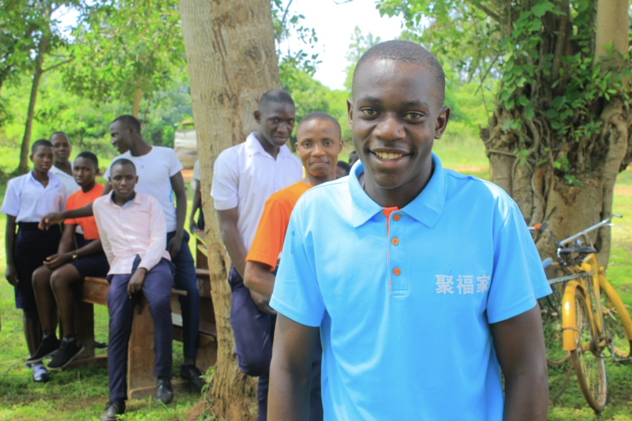 A smiling LeadMinds Africa student leader in smart-casual dress stands in front of a group of his peers.