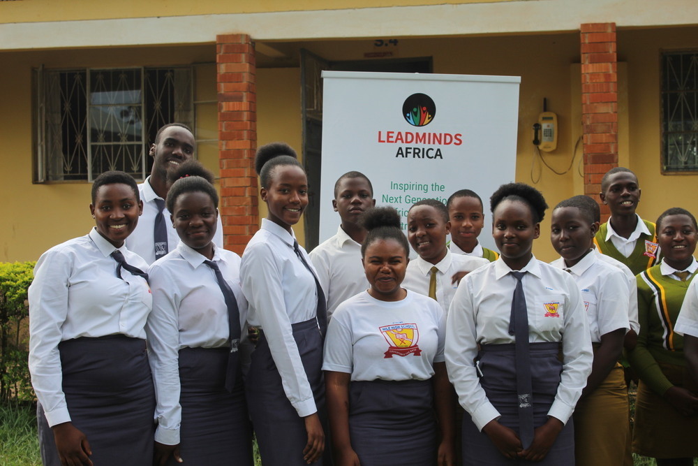 A group of LeadMinds Africa students in sharp uniforms smiles in front of a LeadMinds Africa banner.